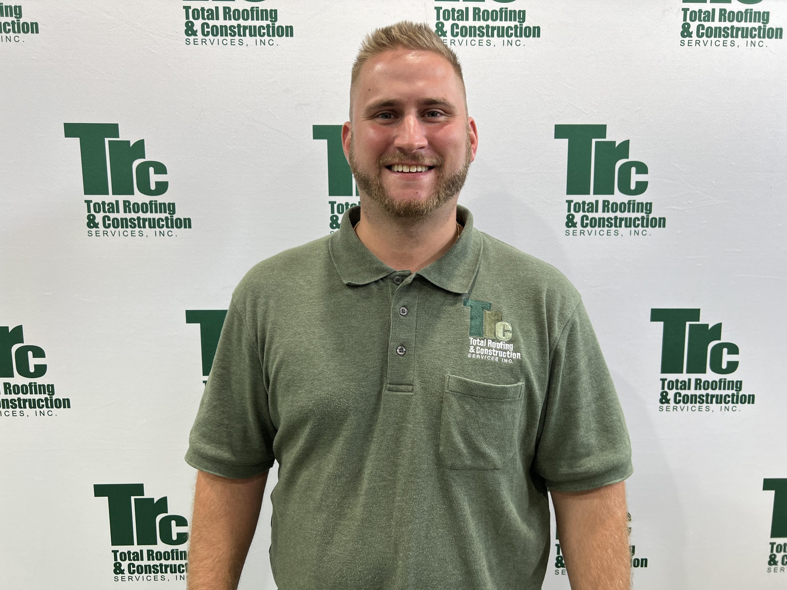 a man stands in front of a wall that says Total Roofing & Constructionservices inc.